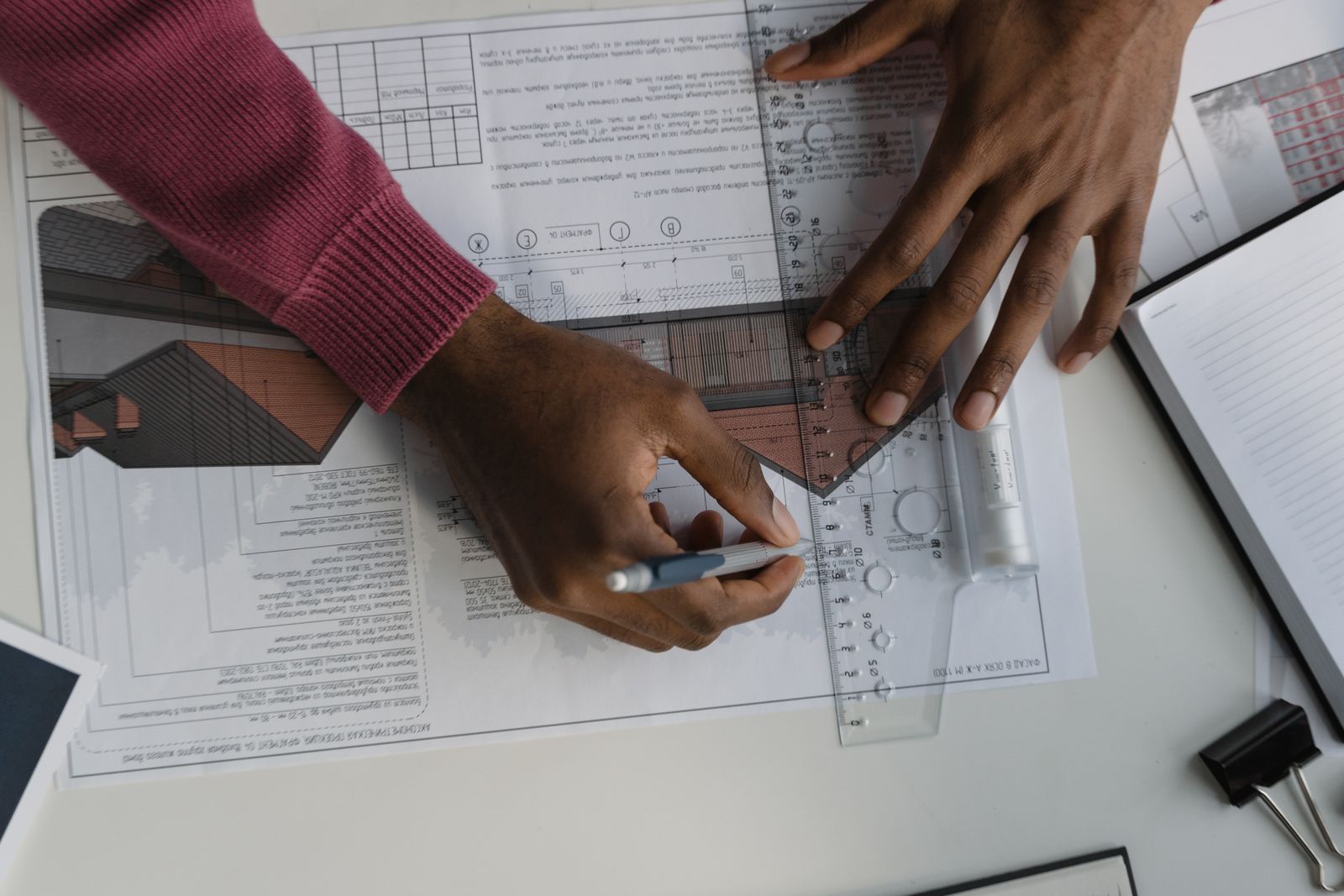 Hands use a ruler and pen on printed architectural plans