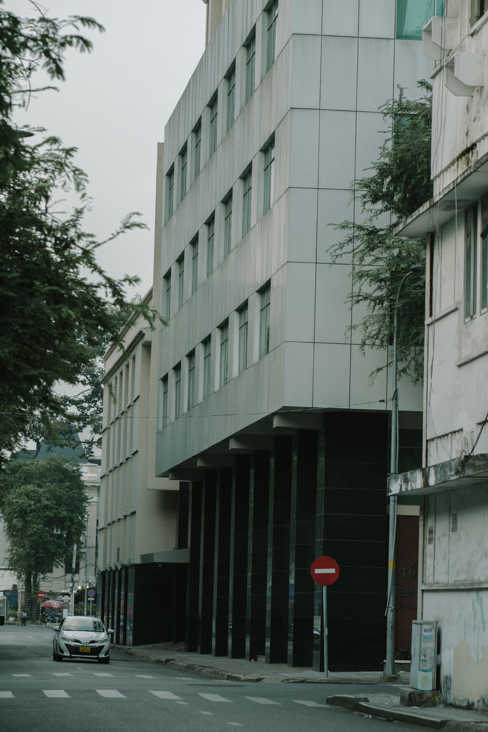 Street-level view looking upward along a modern paneled facade between neighboring buildings