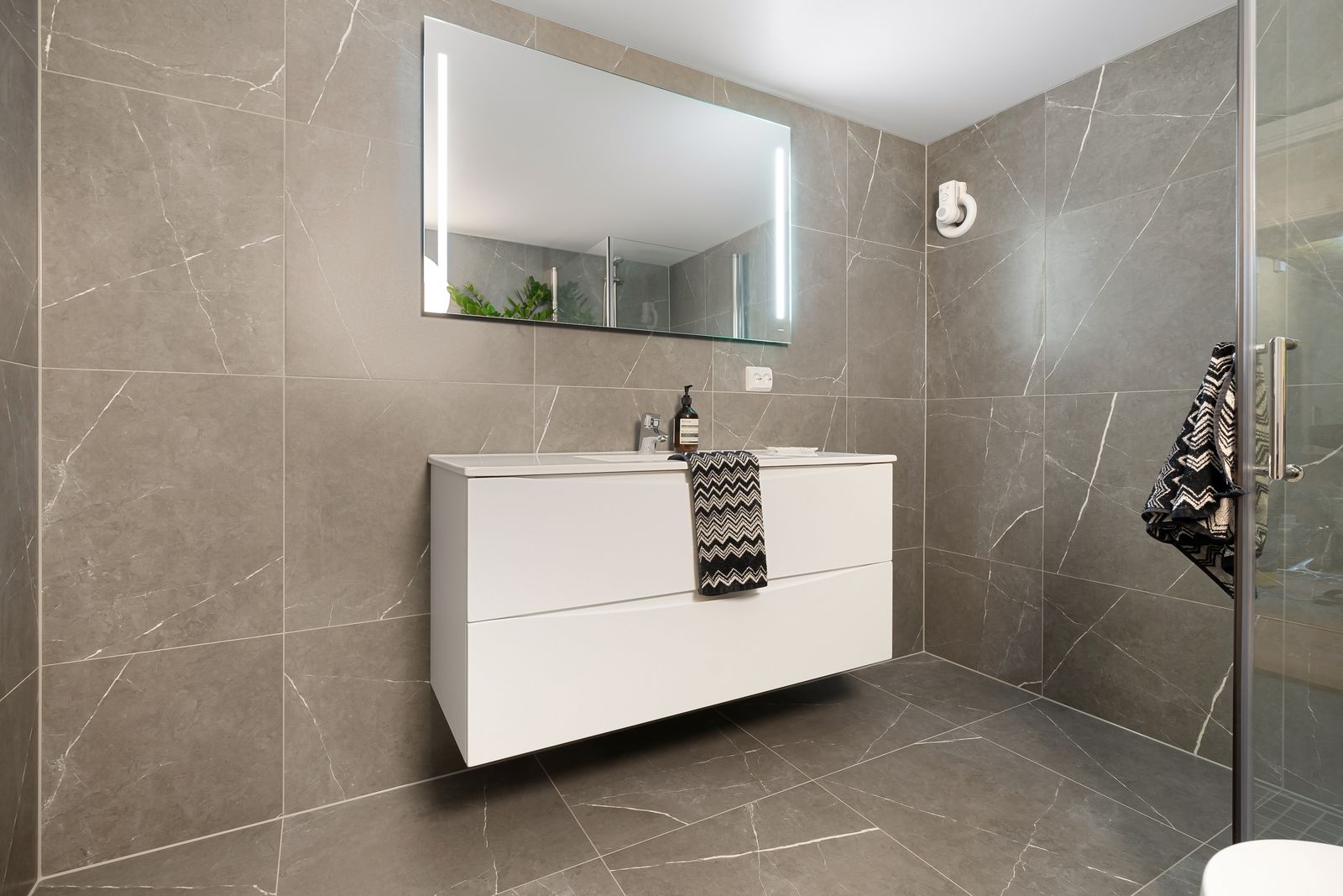 Bathroom vanity and mirror surrounded by gray tiled surfaces