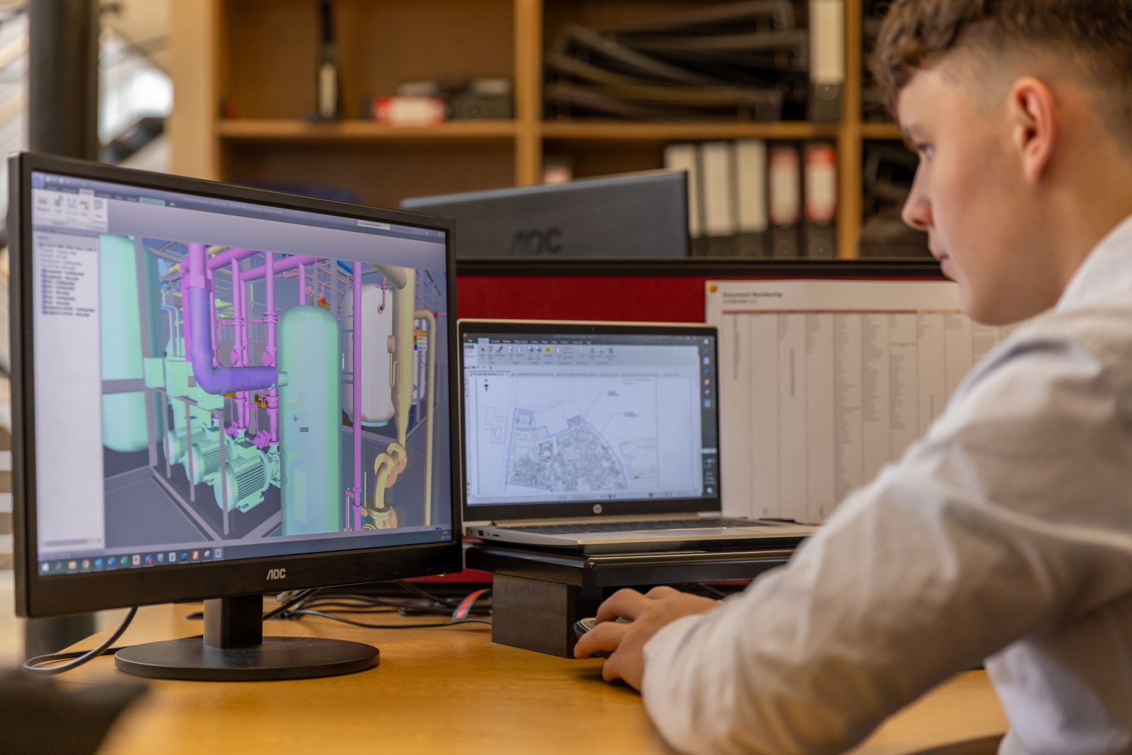 Engineer works with a multicomponent CAD assembly and a technical drawing on two screens