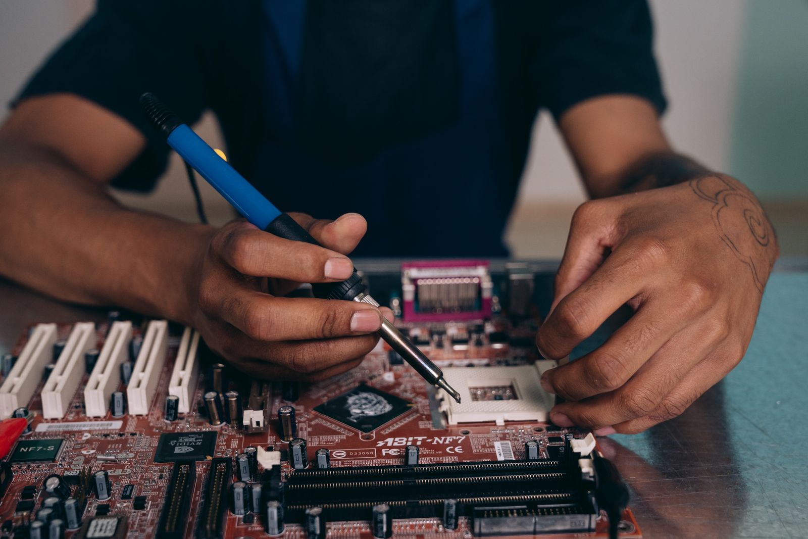 Hands work with a soldering tool over an electronic circuit board