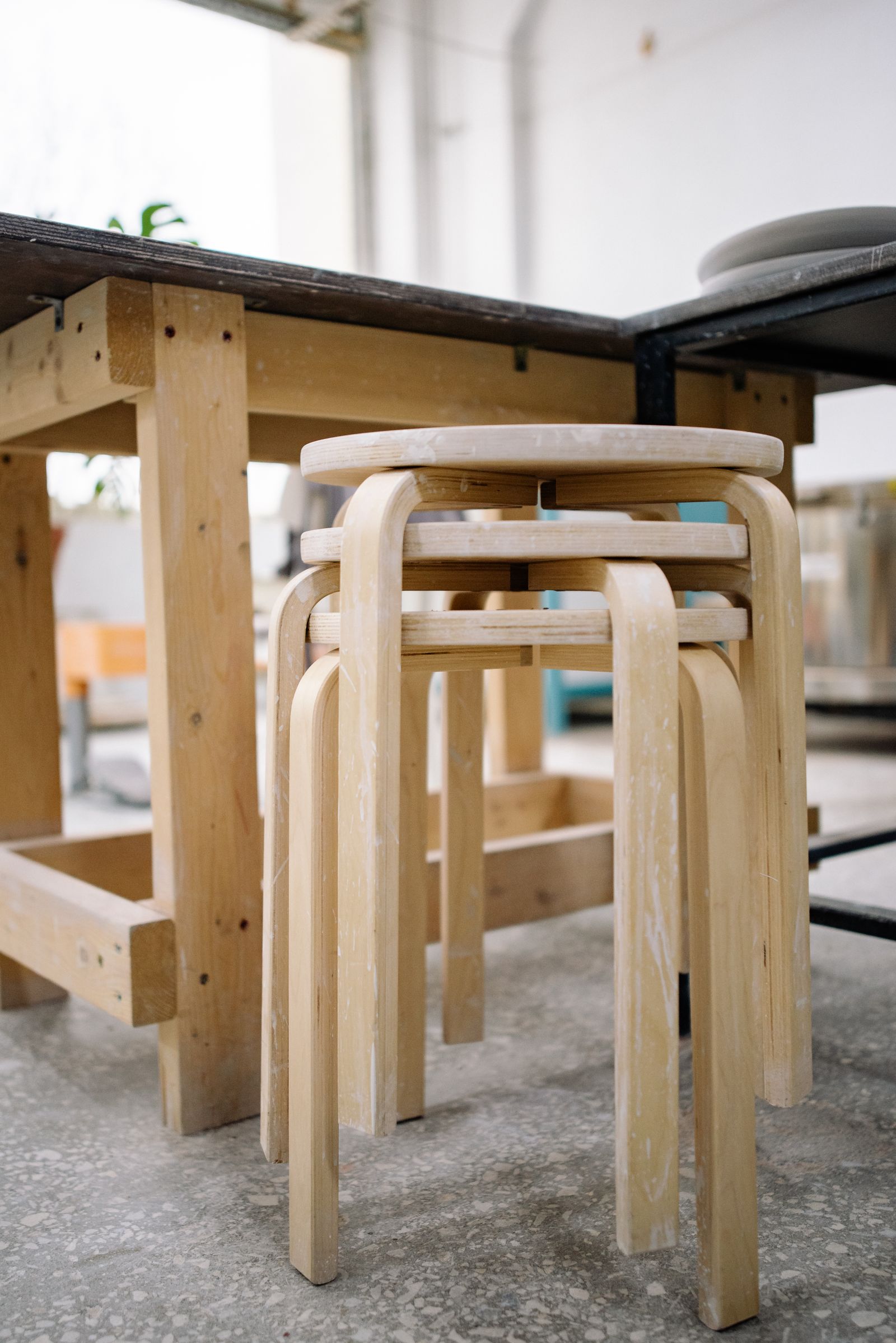 Three round wooden stools stacked beneath a workshop bench