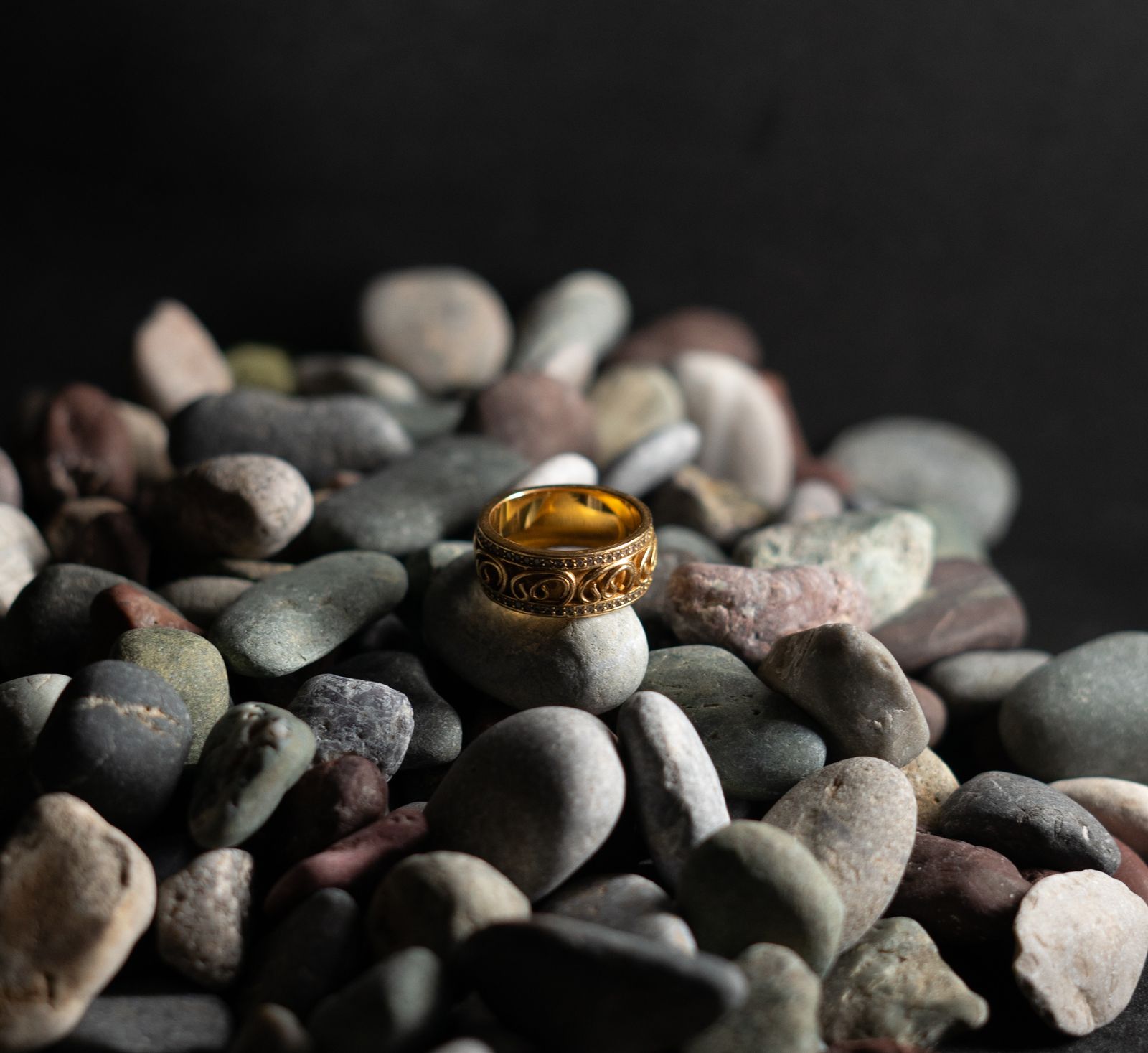 Gold-colored ring with detailed surface resting on stones