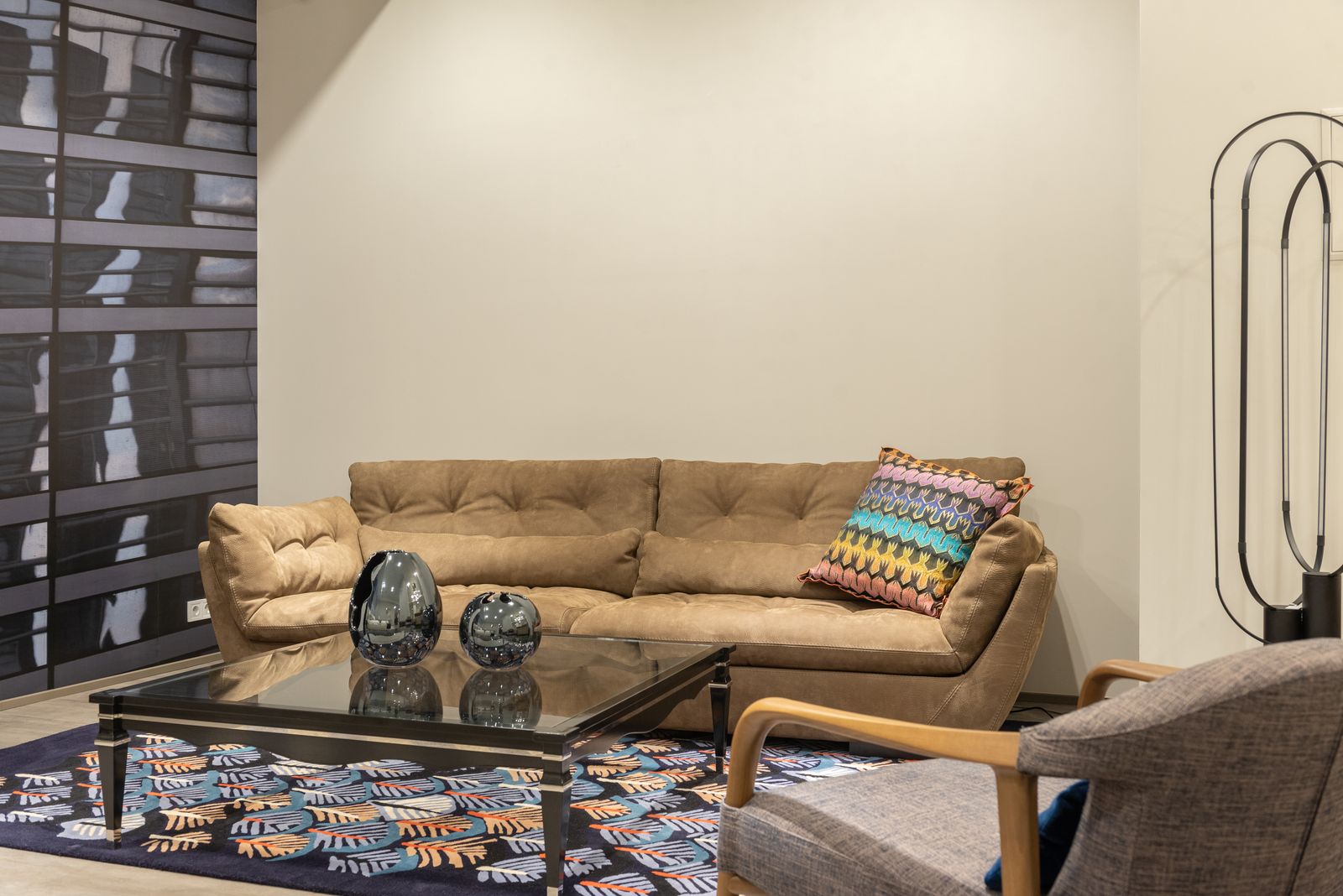 Living room with a tan leather sofa, dark coffee table, patterned rug and a black floor lamp