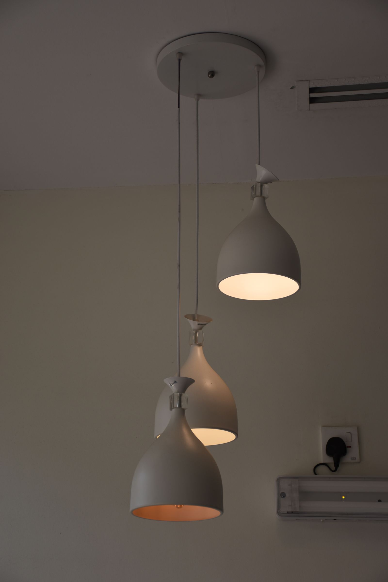 White pendant lights hanging at different depths, with illuminated shades and an air-conditioning unit on the wall