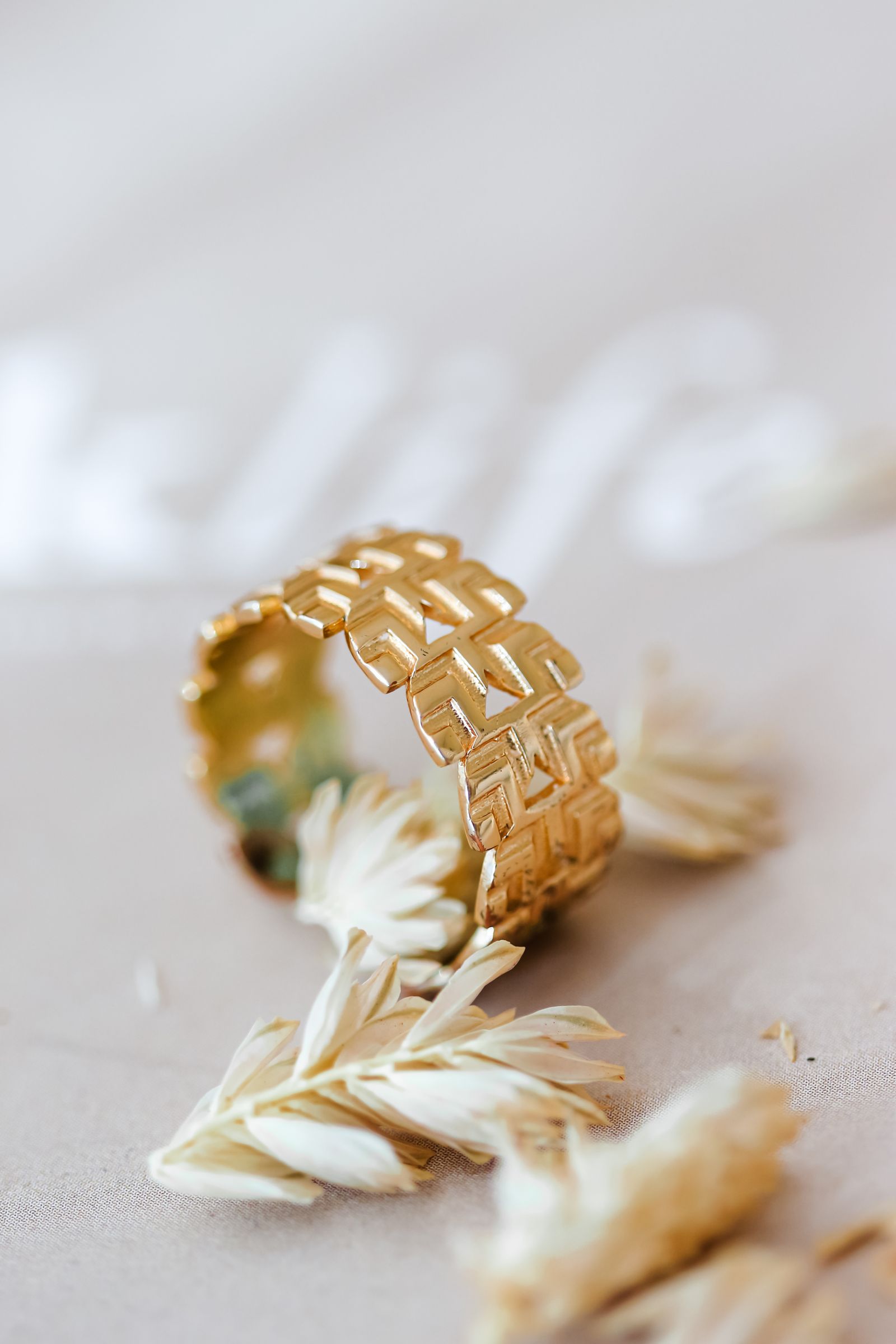Close detail of an ornamental gold-colored ring beside pale flowers