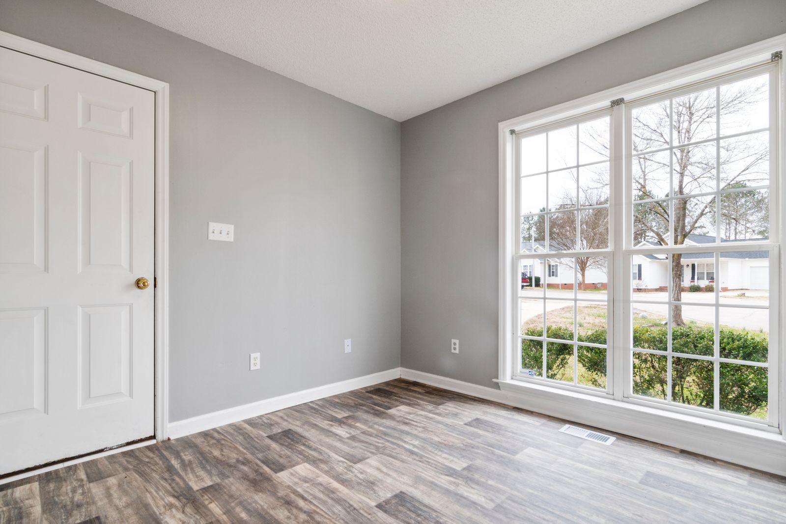 Empty room with a double door, large window, wall outlets and a floor register