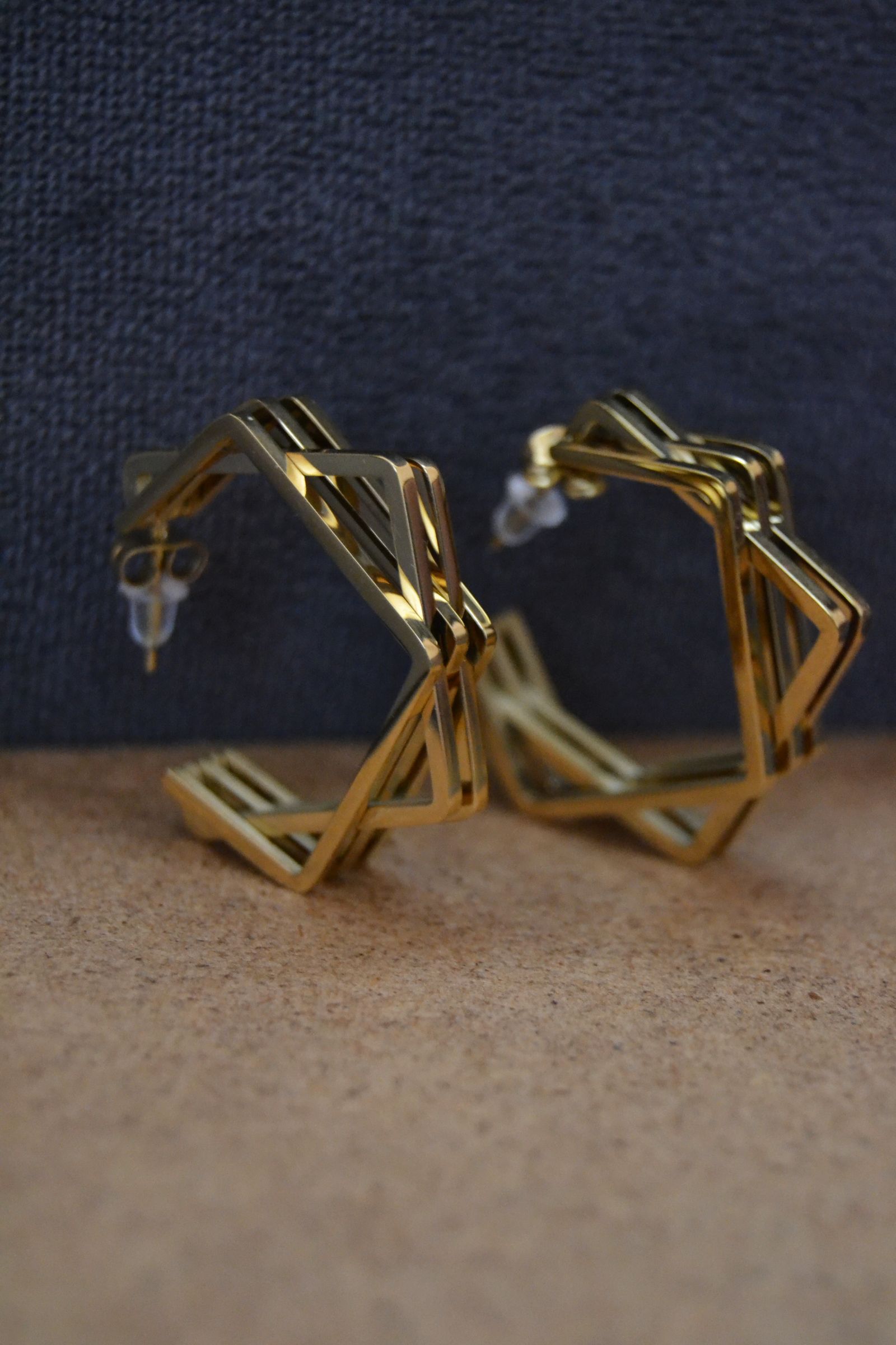 Pair of geometric gold-colored earrings on a textured surface