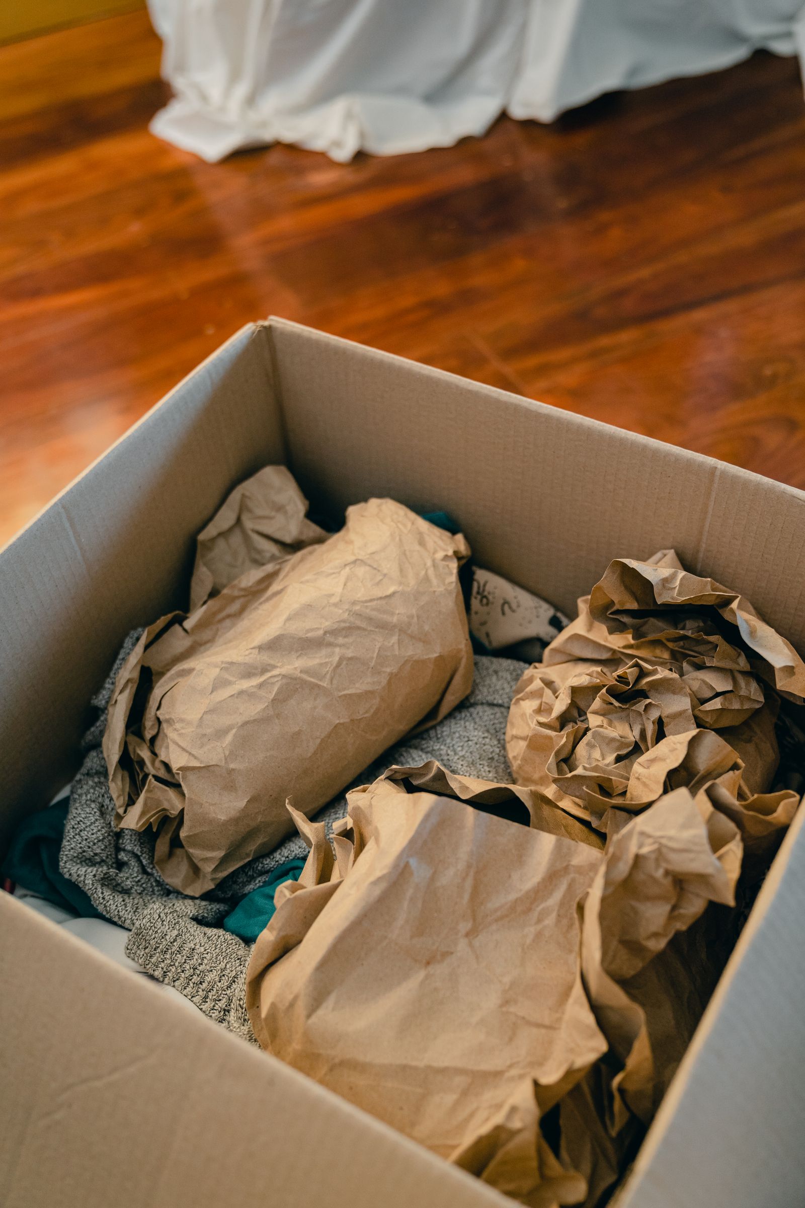 Paper-wrapped objects packed inside an open cardboard box on a wooden floor