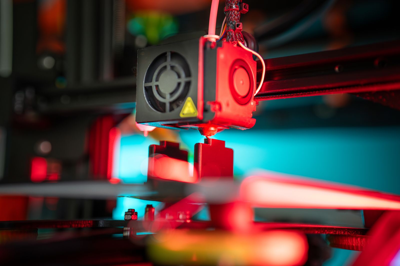 Close-up of a filament printer depositing material onto a red rectangular prototype on its build plate