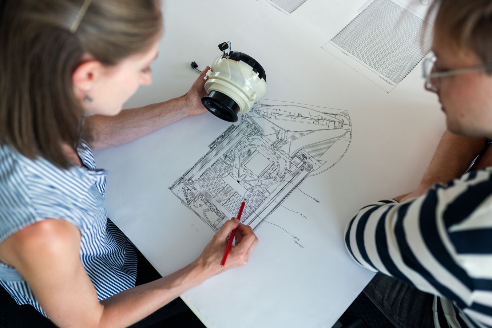 Two engineers compare a physical cylindrical component with a sectional product drawing