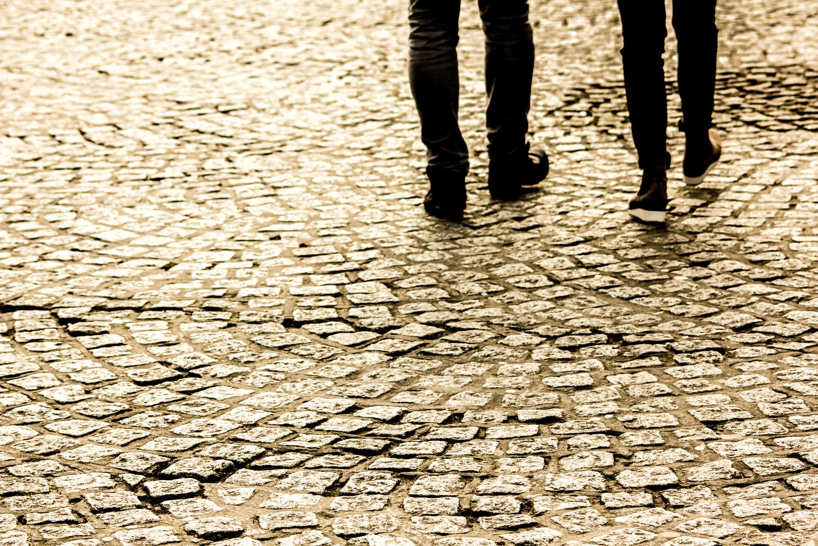 People's legs and feet captured while walking across a cobblestone street