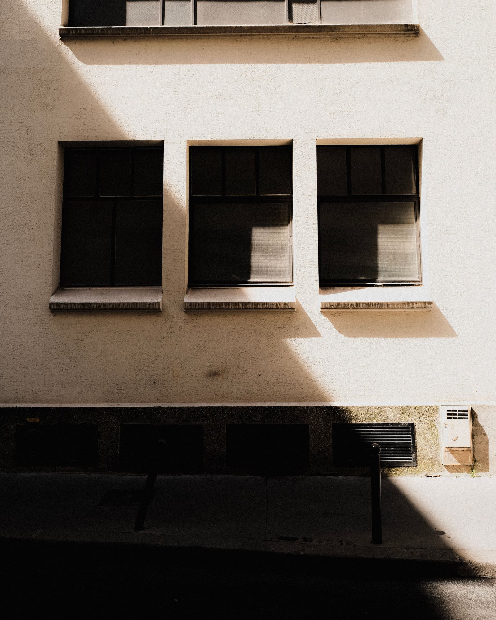 Strong sunlight and diagonal shadows crossing a pale facade with three windows